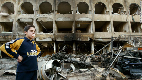 2004年1月28日，一个男孩站在巴格达沙欣酒店前的汽车爆炸现场。（图片来自CNN网站）