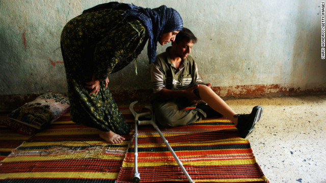 2004年7月17日，20岁的阿桑・哈米德在家中装上了他的新假肢，他的姨妈关切地上前查看。他的左腿膝盖以下在流弹中丧失了。（图片来自CNN网站）