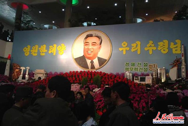 4月15日，朝鲜在位于平壤市中心的“金日成金正日花温室”举行花展进行庆祝。现场人山人海，平壤市民络绎不绝。图为朝鲜已故最高领导人金日成的肖像画旁写着：“永远的太阳，我们的领袖。”