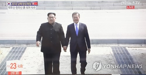 在韩朝边境板门店，韩国总统文在寅（右）同朝鲜最高领导人金正恩携手共同跨过军事分界线。韩联社/韩联社TV截图 