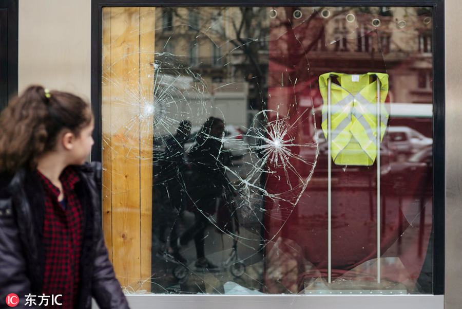 当地时间2018年12月2日，法国巴黎，“黄背心”示威骚乱过后，巴黎街头一片狼藉，一名女子走过被砸碎的商店窗前。图为东方IC版权作品  请勿转载