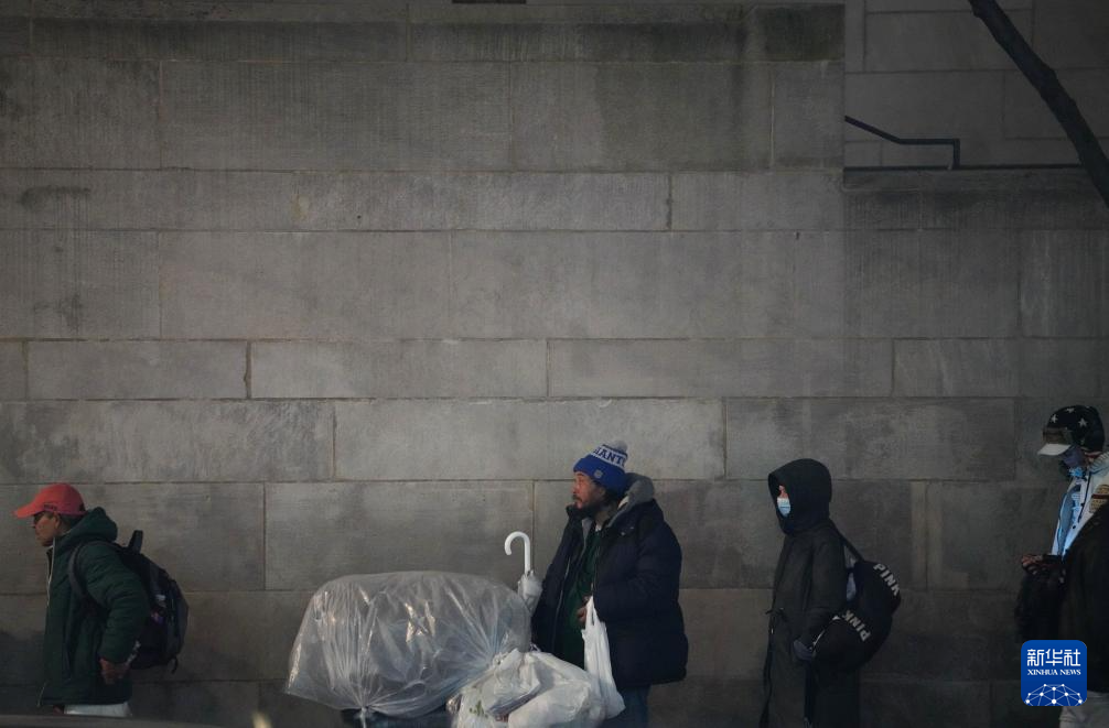 12月17日，在美国纽约曼哈顿的一处救助点，人们排队等待领取免费晚餐。新华社记者 张凤国 摄