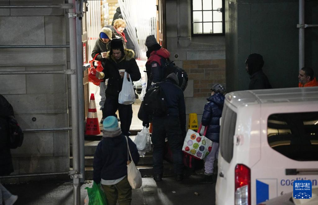 12月17日，在美国纽约曼哈顿，人们拿着免费晚餐走出救助点。新华社记者 张凤国 摄