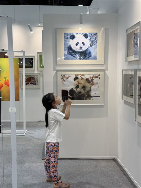 一名泰国小女孩在“绿动中国:熊猫、草木与微距生灵的生态叙事”展览现场拍摄熊猫照片。 中国出版代表团供图