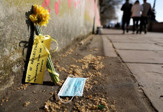 这是3月27日在英国伦敦国家新冠纪念墙边拍摄的花束和口罩。花束旁的字条上写着“纪念在疫情中失去生命的人们”。新华社记者李颖摄