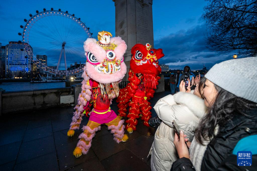 2月16日晚，在英国首都伦敦，演员在亮起红色灯光的“伦敦眼”前表演舞狮。新华社发（史蒂芬·程摄）