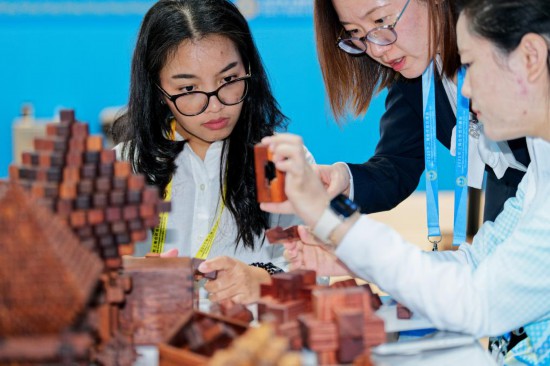 一名印度尼西亚记者（左）在2025年上海合作组织峰会新闻中心了解传统木工榫卯技艺。新华社记者张笑宇摄